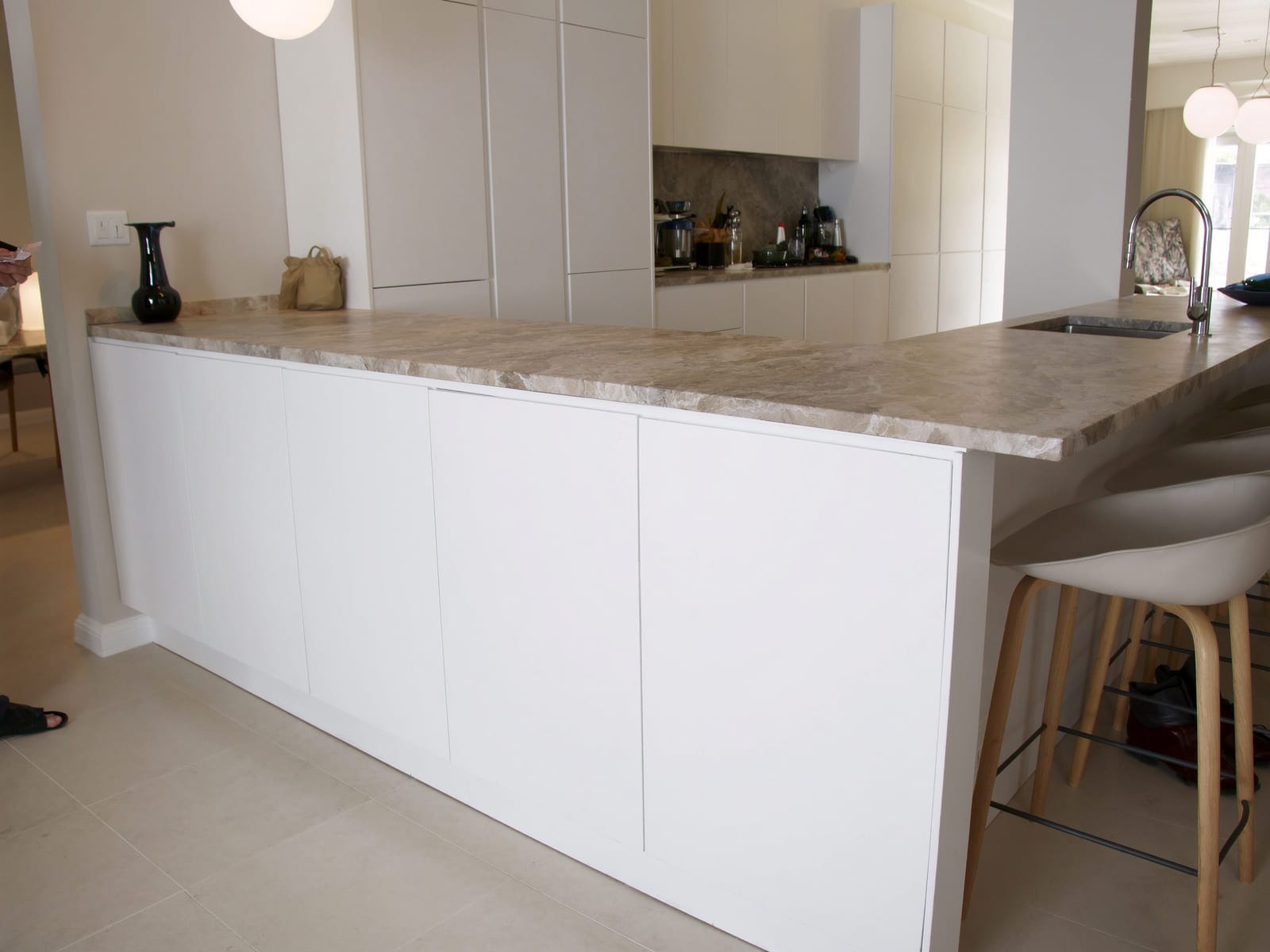 A kitchen island with high gloss white melamine cabinet fronts, a thick stone patterned laminate worktop, bar stools tucked underneath and pendant lights above. Illustrative concept visual, not a real photograph.