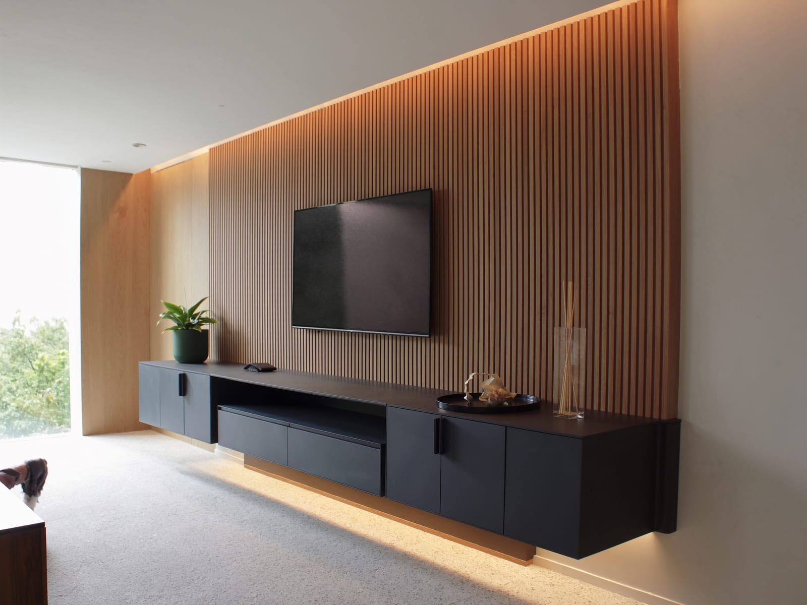 A living room media wall with a floating television unit in matte charcoal melamine below a vertical fluted timber panelled feature wall in warm oak. Illustrative concept visual, not a real photograph.