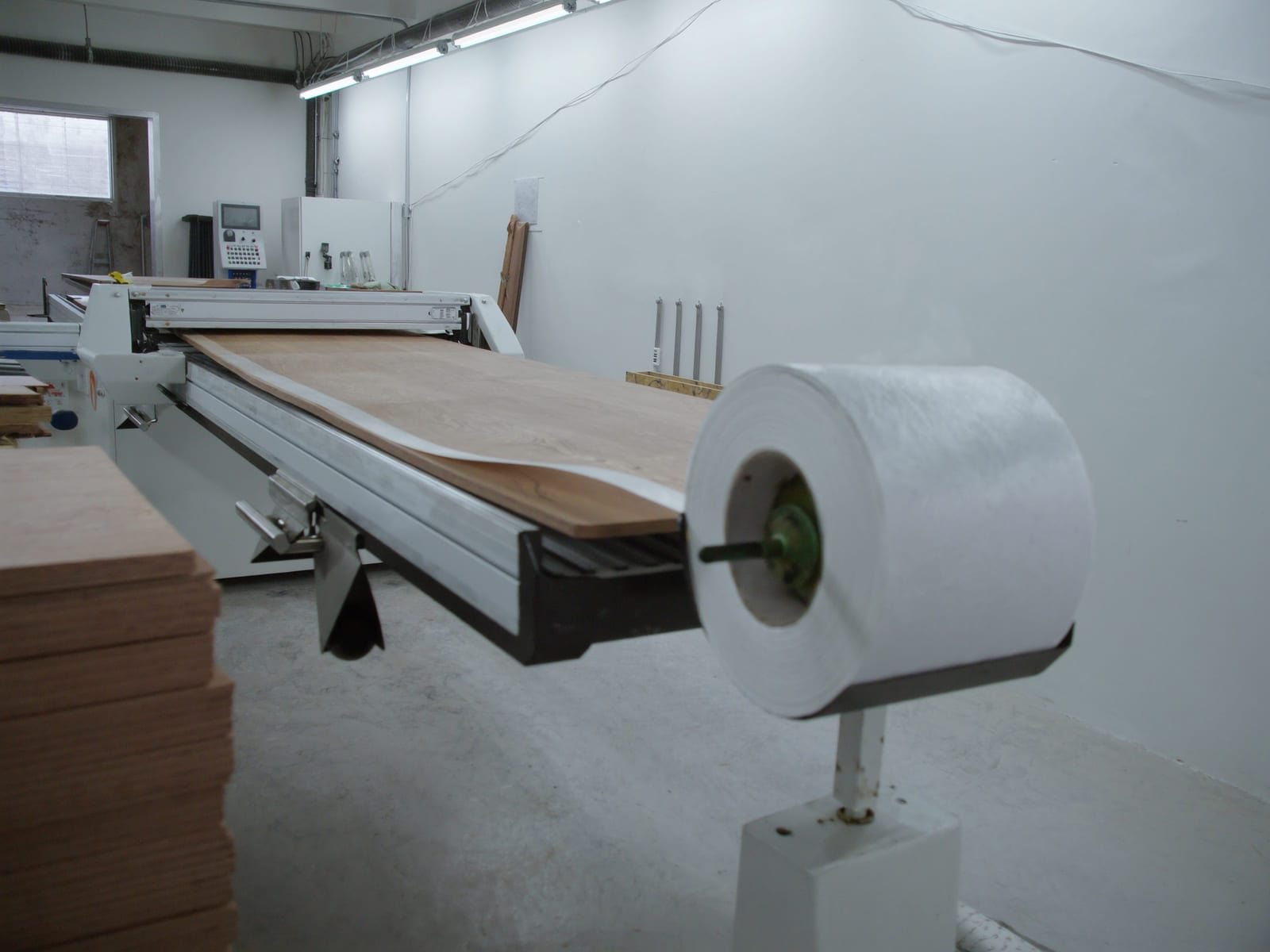 An industrial edge banding machine with a woodgrain melamine panel emerging from it, a roll of matching edge tape mounted above, and finished edged panels stacked beside it. Illustrative concept visual, not a real photograph.
