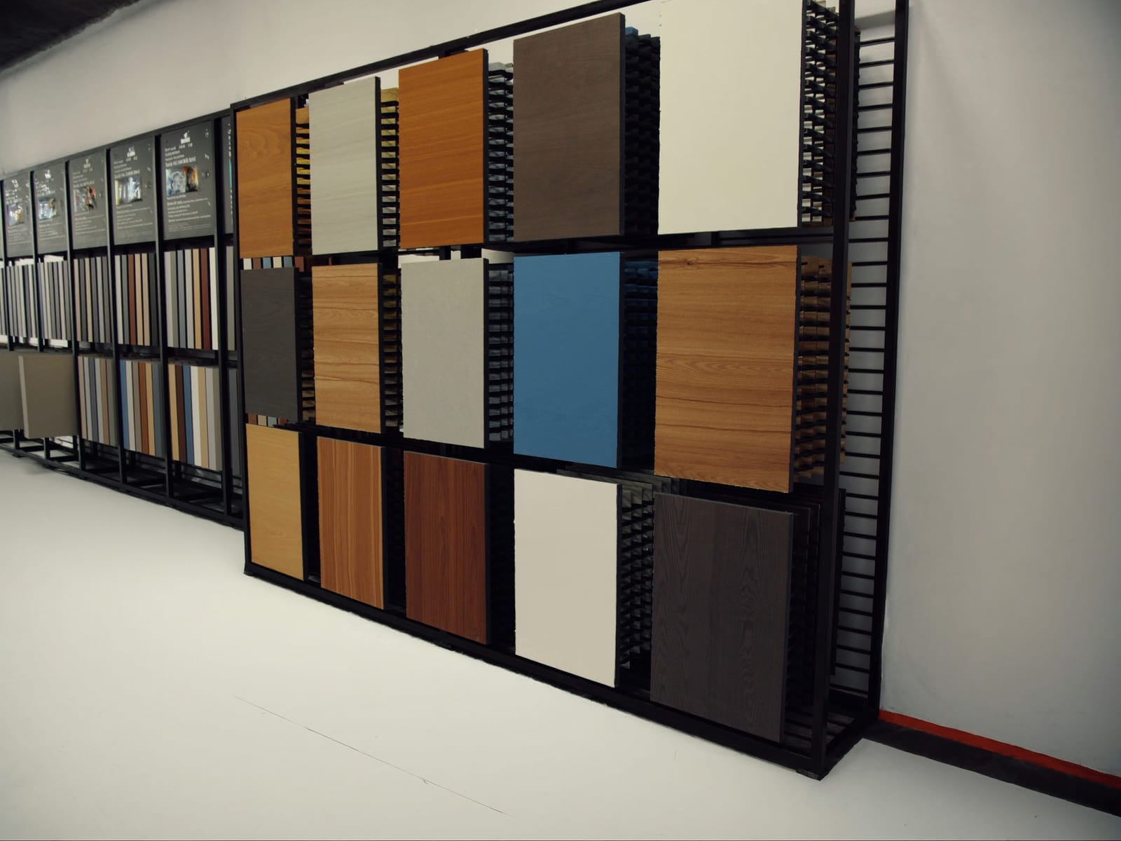 A wall mounted display of small melamine decor samples in many colours and woodgrains, arranged in a grid above a counter with loose samples fanned out on it. Illustrative concept visual, not a real photograph.